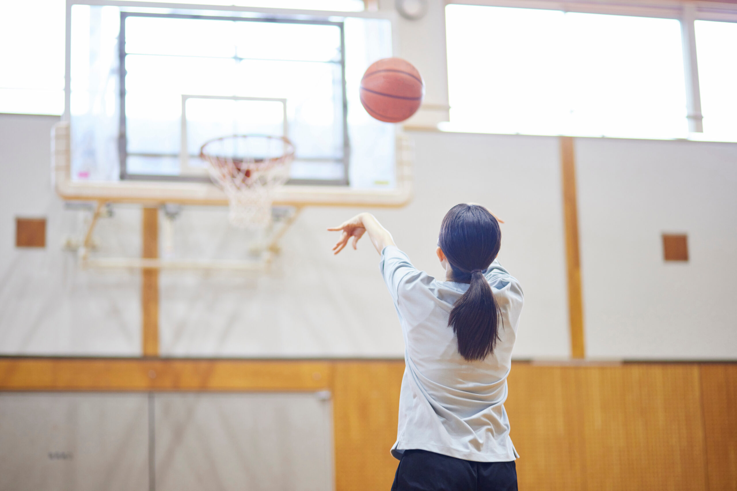 体育館でバスケットボールをしている女性の後ろ姿
